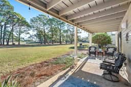 Covered back terrace with string lights, wicker seating, and sweeping golf-course views — the ideal spot to ease into the morning